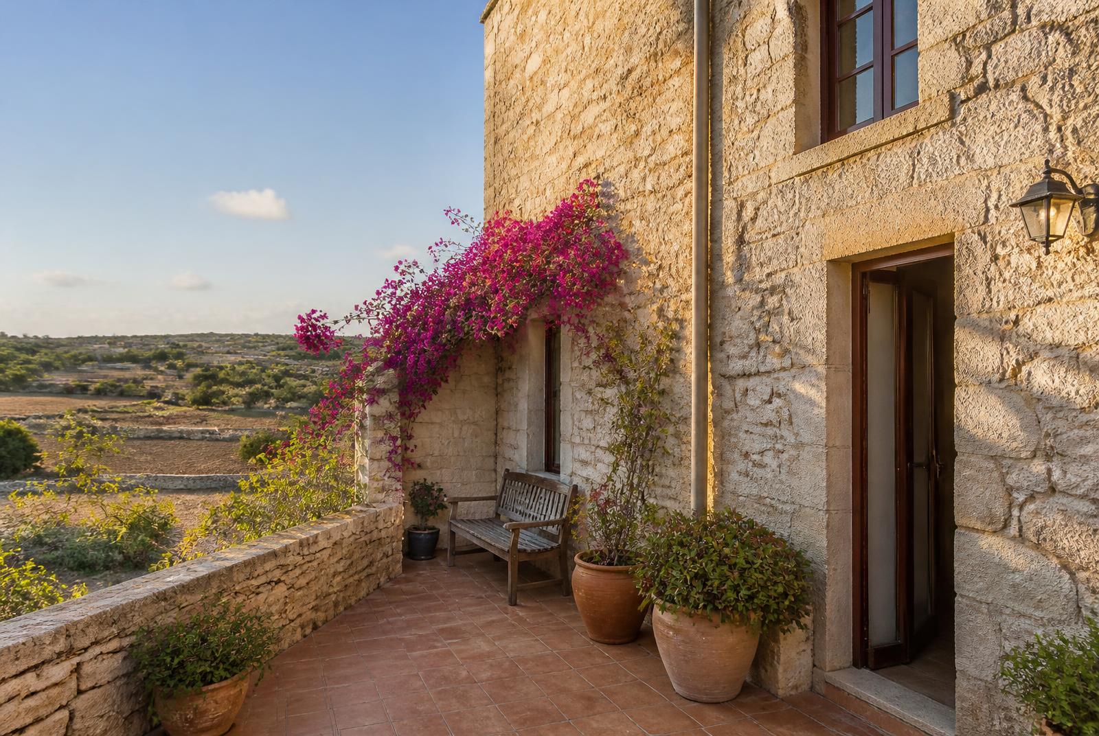 Terras van een stenen woning op Gozo met bougainville en uitzicht over droge velden
